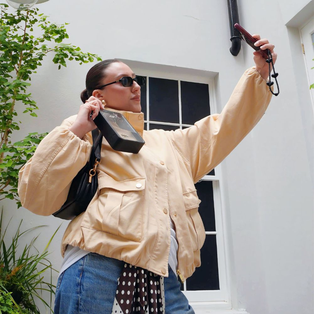 Woman holding a Noir (black) Sips water bottle whilst taking a picture of her coordinated outfit and bottle.