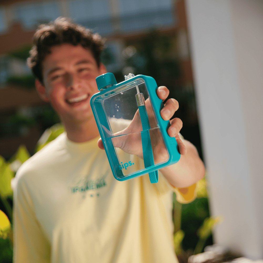 Close up of a Sips Water Bottle in Teal being held by a man in a yellow top on holiday.