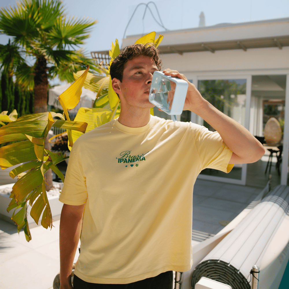 Man drinking from a Sips water bottle in bubblegum (light blue) whilst stood in front of the pool.
