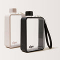 Two Sips water bottles on a clean off-white background, one in Oyster grey ( light grey) colour and the other in Noir (black) with a  textured protective bumper and a black wrist strap.