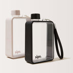 Two Sips water bottles on a clean off-white background, one in Oyster grey ( light grey) colour and the other in Noir (black) with a  textured protective bumper and a black wrist strap.