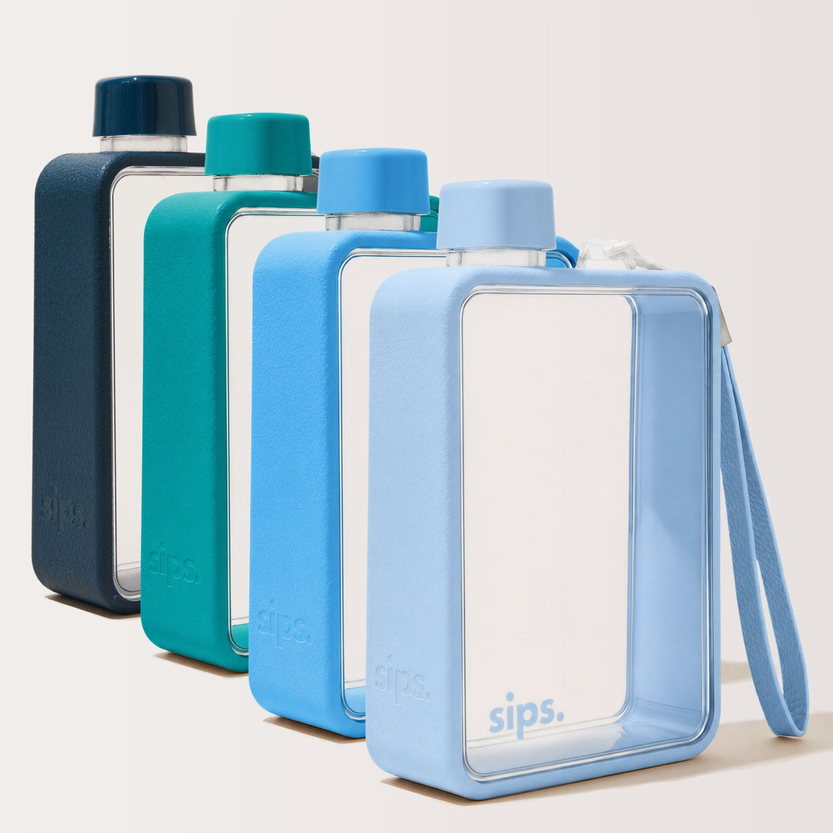 Four rectangular Sips water bottles with clear bodies and coloured protective bumpers in space blue (dark blue), teal, sky and bubblegum (light blue) arranged in a row on a plain background. Each bottle has a matching cap and a wrist strap.