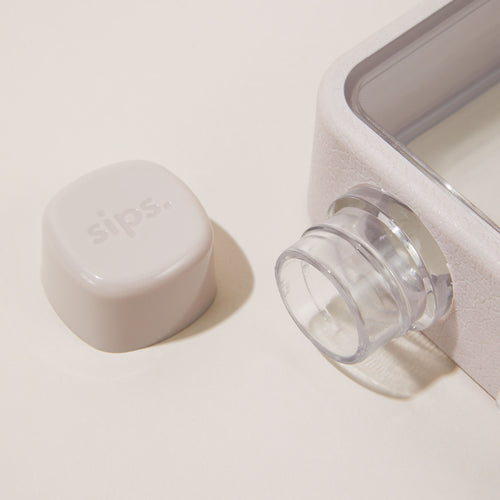 Close up of a Sips Water Bottle in Oyster Grey with a screw top lid and branded carry strap.