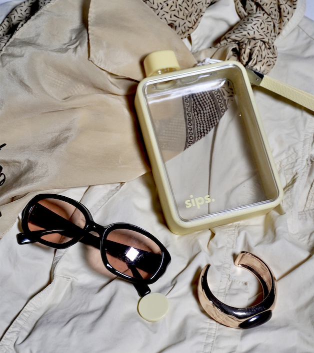 Sips Water bottle in Pastel Yellow on a bunfabric background with sunglasses and a bangle.